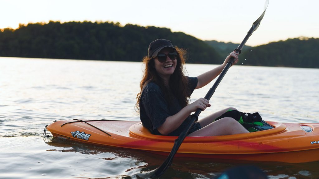 A woman in sunglasses with a big smile kayaking down the Bow River.