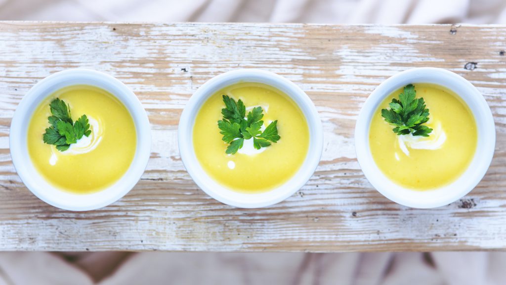 three bowls of potato leek soup artfully arranged on a white washed wood plank