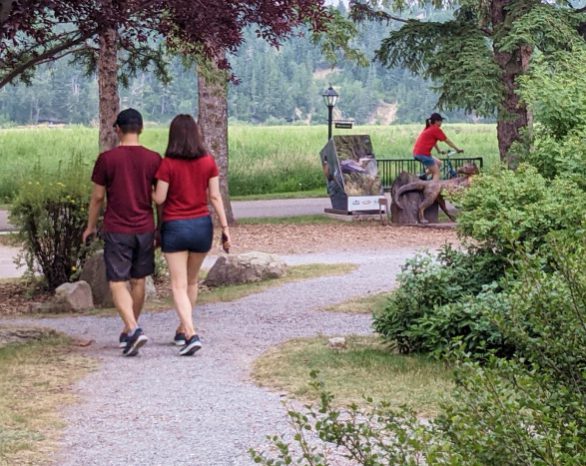 a couple wearing red shirts walking through fish creek park with a cyclist in the background