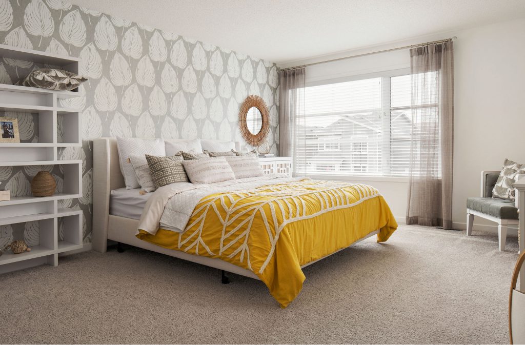 bedroom with a leaf wallpaper feature wall, light furniture, and yellow comforter