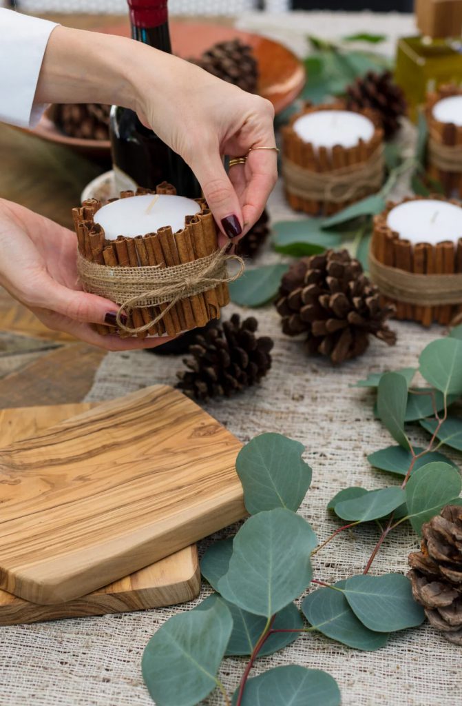 woman's hands holding a candle center piece with cinnamon sticks