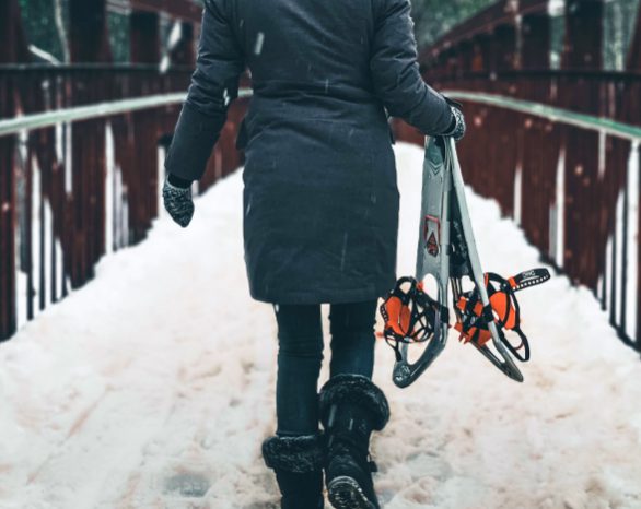 person walking across a bridge in fish creek park carrying snowshoes