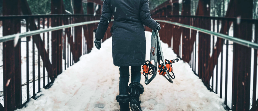 person walking across a bridge in fish creek park carrying snowshoes