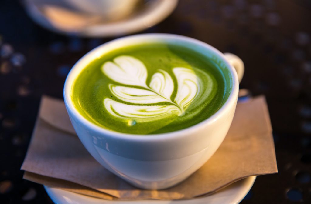 a green, matcha latte in a white mug with a floral latte art design on top