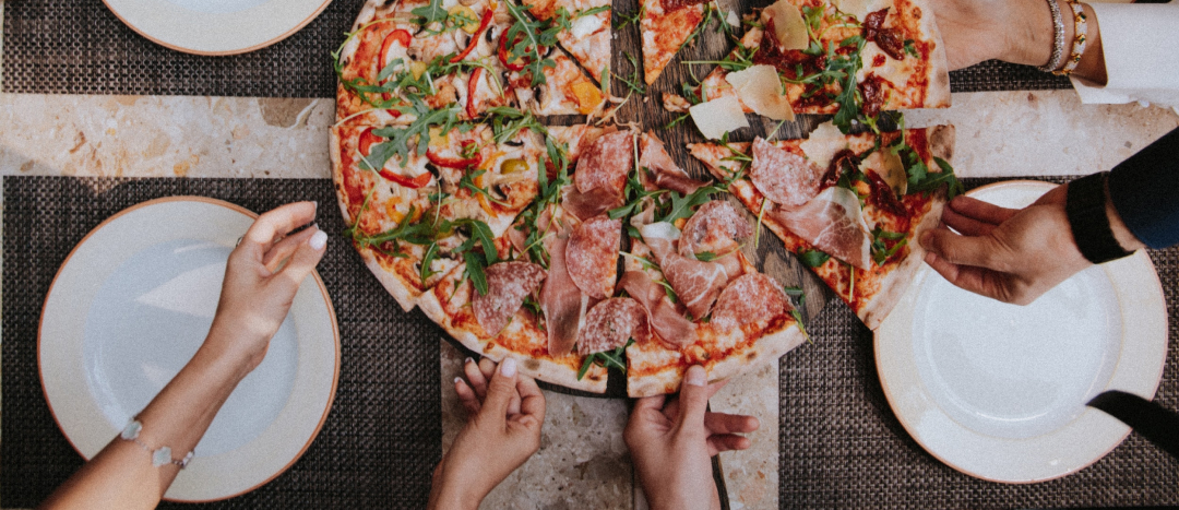 an overhead photo of a pizza and 5 hands reaching in to grab a slice